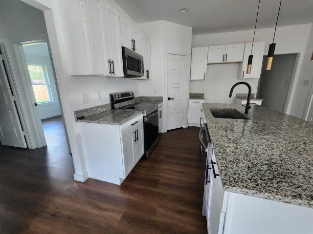 562 Jonelle Avenue Dallas, TX 75217 - Photo 5 of 20 Kitchen with light stone countertops, white cabinets, stainless steel appliances, dark wood-style flooring, and a kitchen island with sink