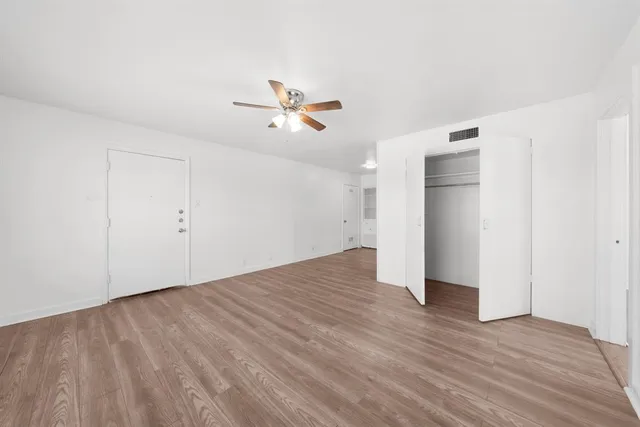 an empty room with wooden floor chandelier fan and windows