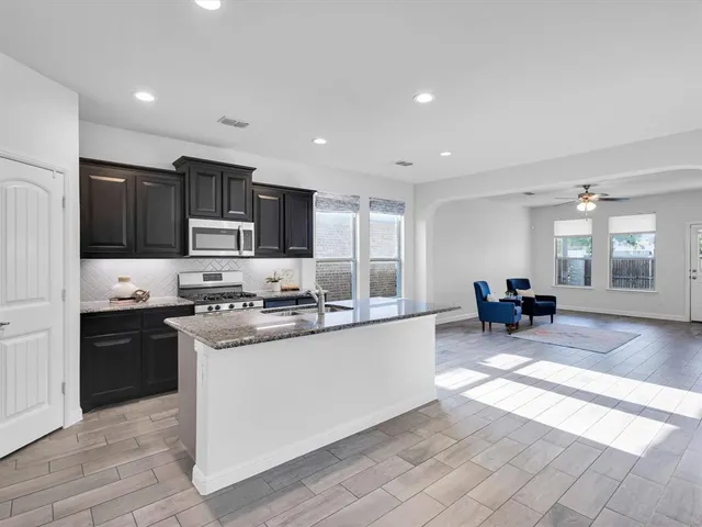 a kitchen with stainless steel appliances granite countertop a stove top oven a sink dishwasher a dining table and chairs with wooden floor