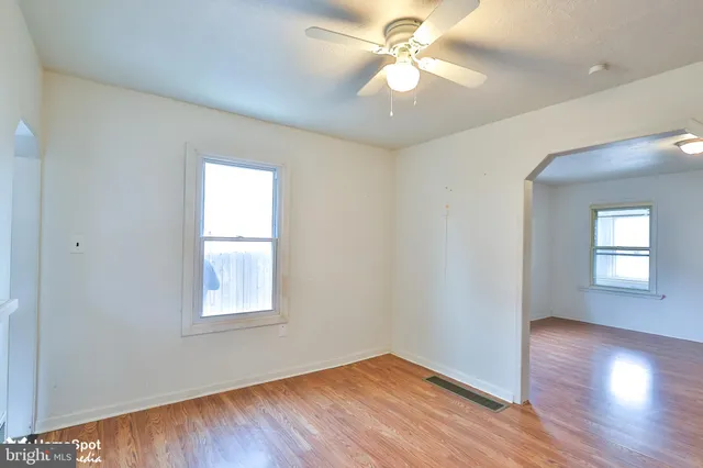 an empty room with wooden floor ceiling fan and windows