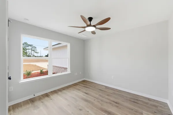 an empty room with wooden floor chandelier fan and windows