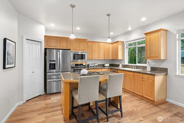 a kitchen with stainless steel appliances granite countertop a refrigerator a sink dishwasher a stove and white cabinets with wooden floor