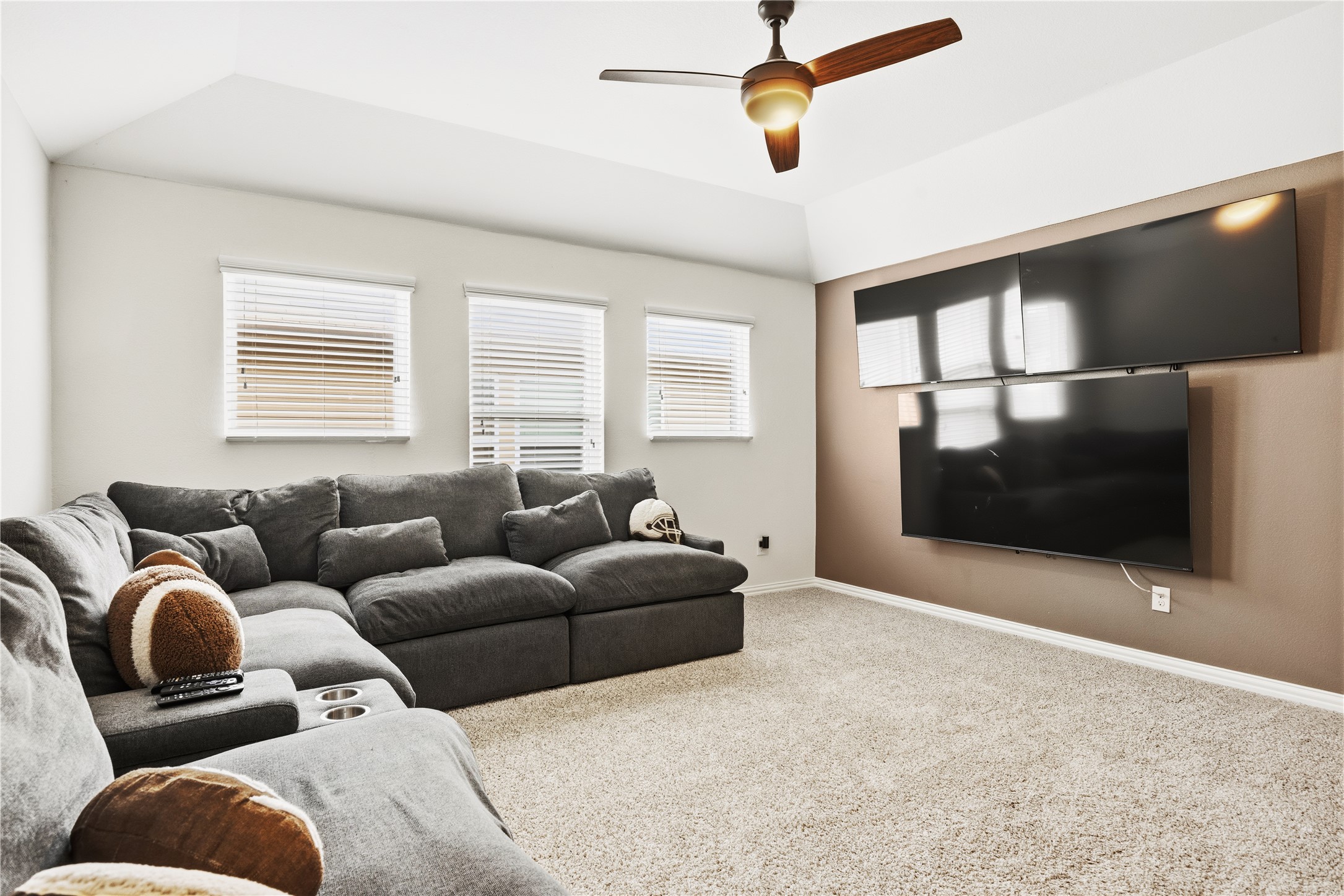 486 Pond View Pass Buda, TX 78610 - Photo 19 of 39 Carpeted room featuring a ceiling fan with integrated lighting, three windows with blinds, a vaulted ceiling, and a wall with multiple mounted screens