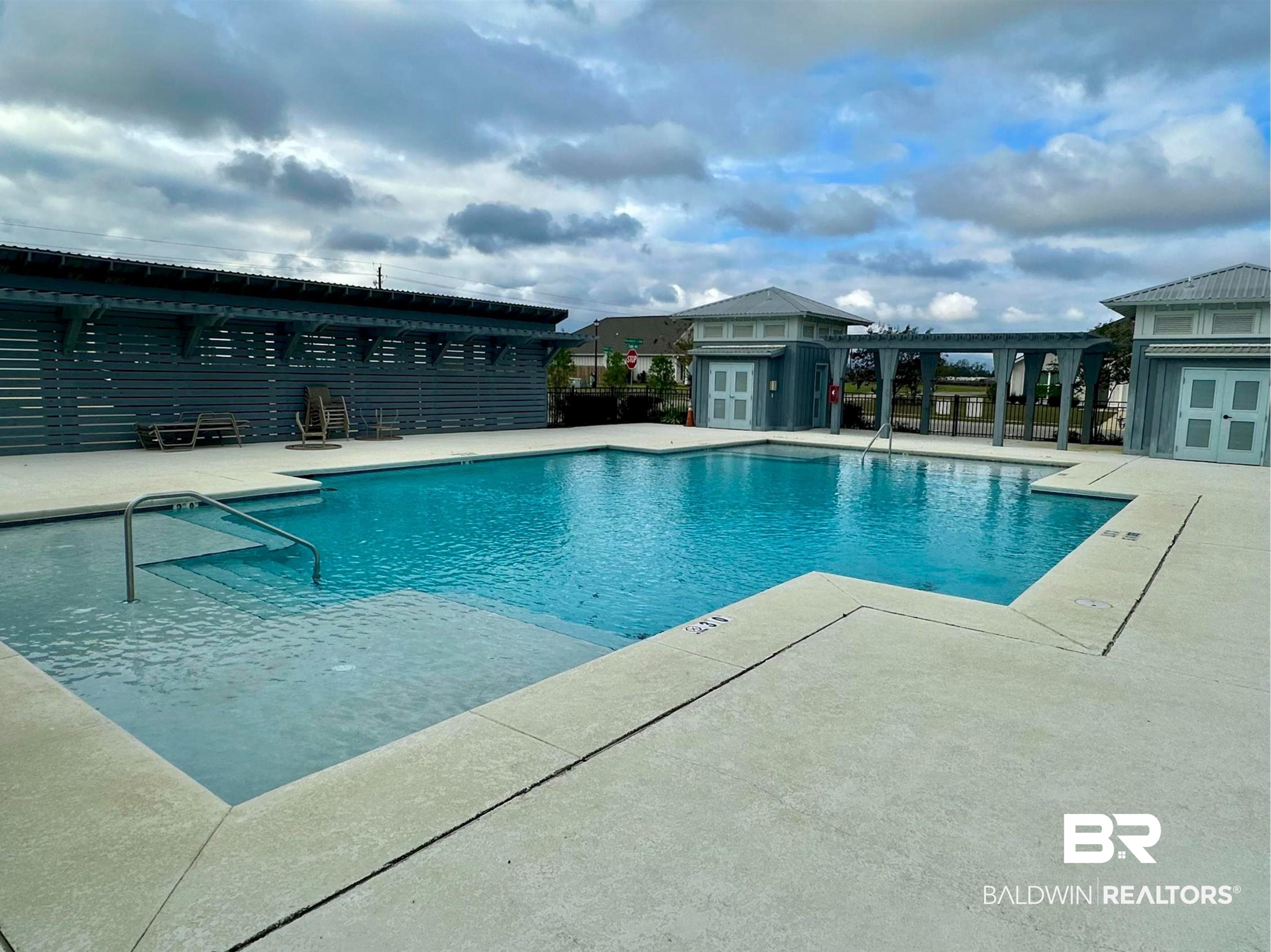 1040 Hayward Loop Foley, AL 36535 - Photo 33 of 35 Spacious community pool featuring concrete decking, a shallow entry area with handrail, and an adjacent shaded pergola structure