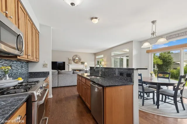 a kitchen with stainless steel appliances granite countertop a stove top oven a sink a dining table and chairs with wooden floor