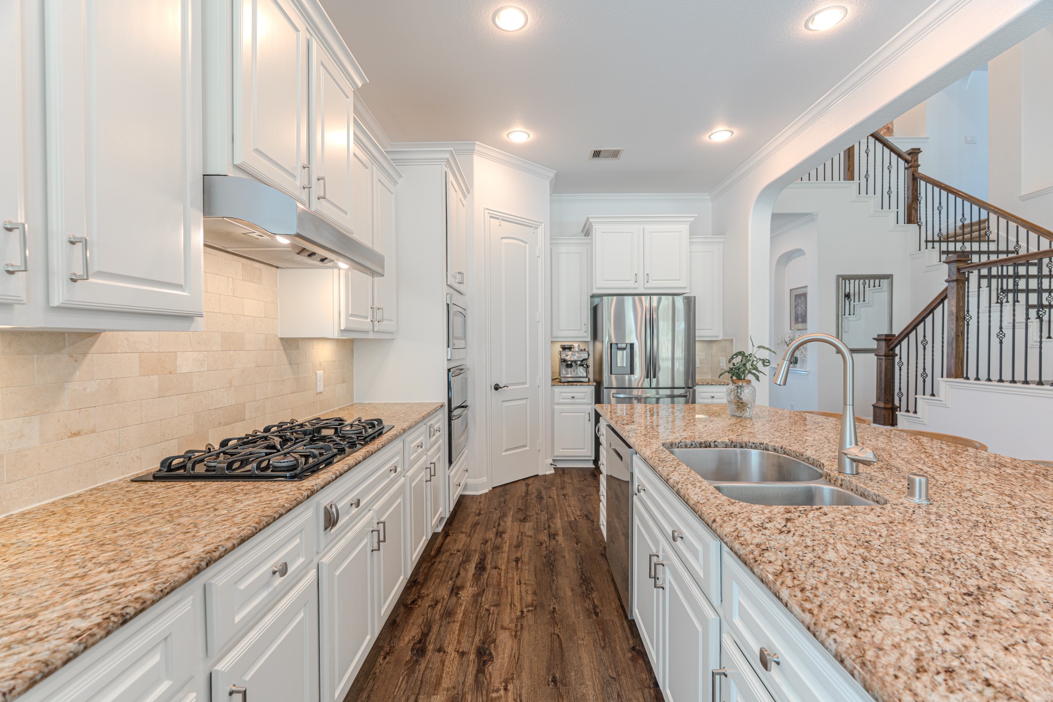 30 Fury Ranch Place The Woodlands, TX 77375 - Photo 17 of 47 This photo showcases a spacious, modern kitchen with granite countertops, white cabinetry, and stainless steel appliances. The open layout includes a large island with a double sink, and the dark hardwood floors add warmth. A staircase with elegant railings is visible in the background, enhancing the home's inviting design.