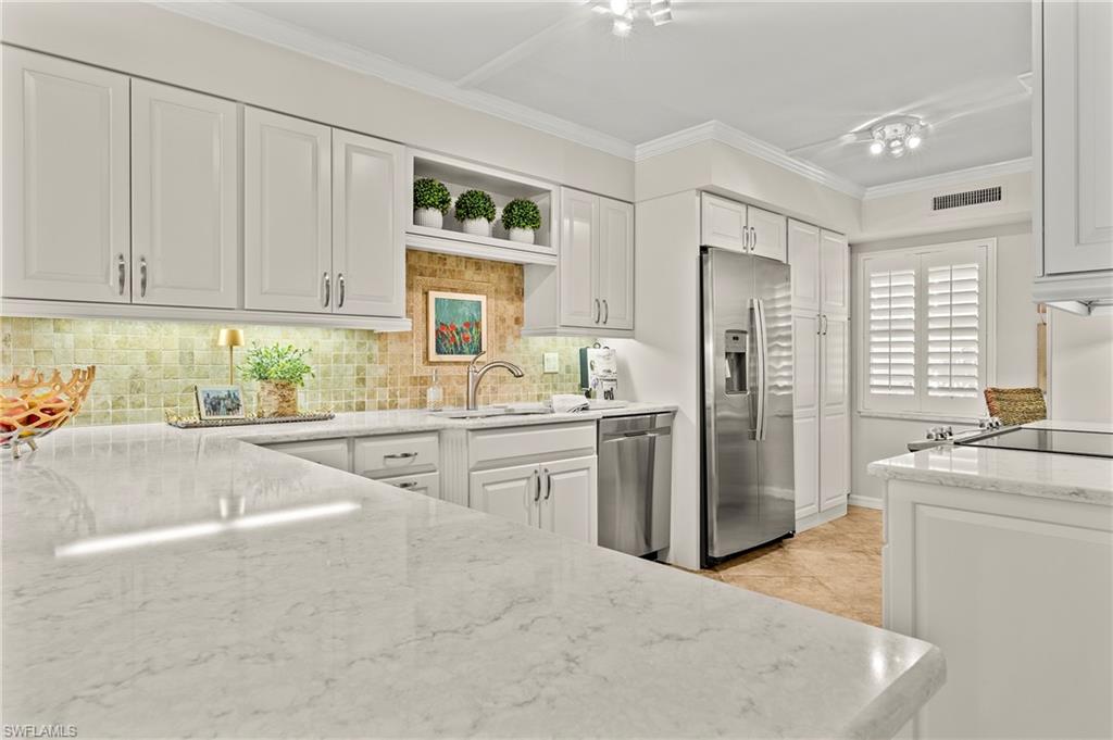 Kitchen with white cabinets, sink, backsplash, light stone countertops, and appliances with stainless steel finishes