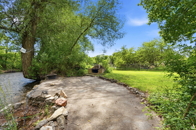 778 East 200 North Logan, UT 84321 - Photo 5 of 43 Riverside concrete patio with a built-in outdoor grill, bordered by mature trees and a manicured lawn