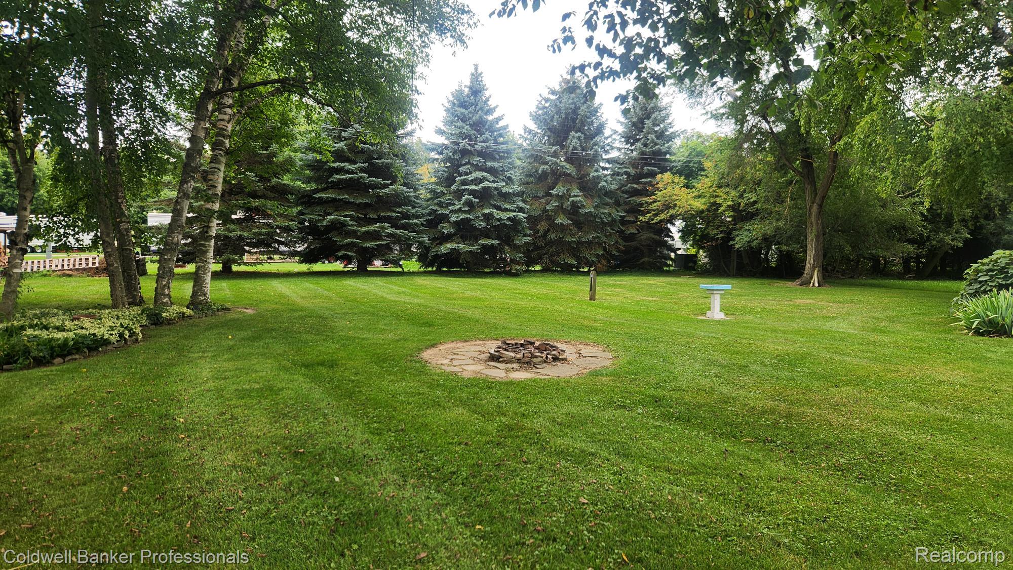 3300 Pointe Aux Barques Road Port Austin, MI 48467 - Photo 24 of 27 Expansive green lawn with mature trees and a stone-lined fire pit