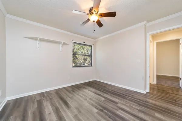 a view of an empty room with wooden floor and ceiling fan