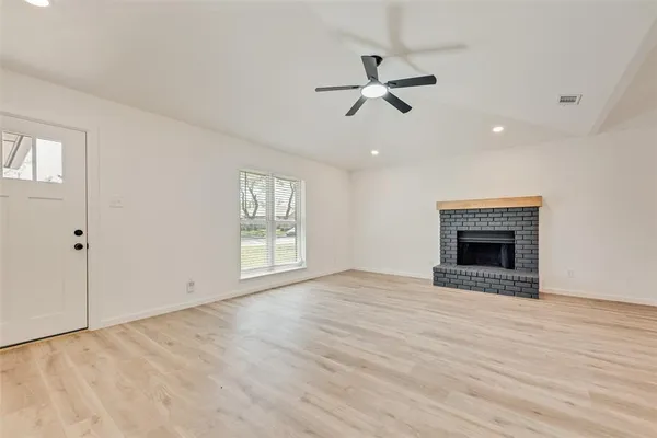 a view of an empty room with wooden floor fireplace and a window
