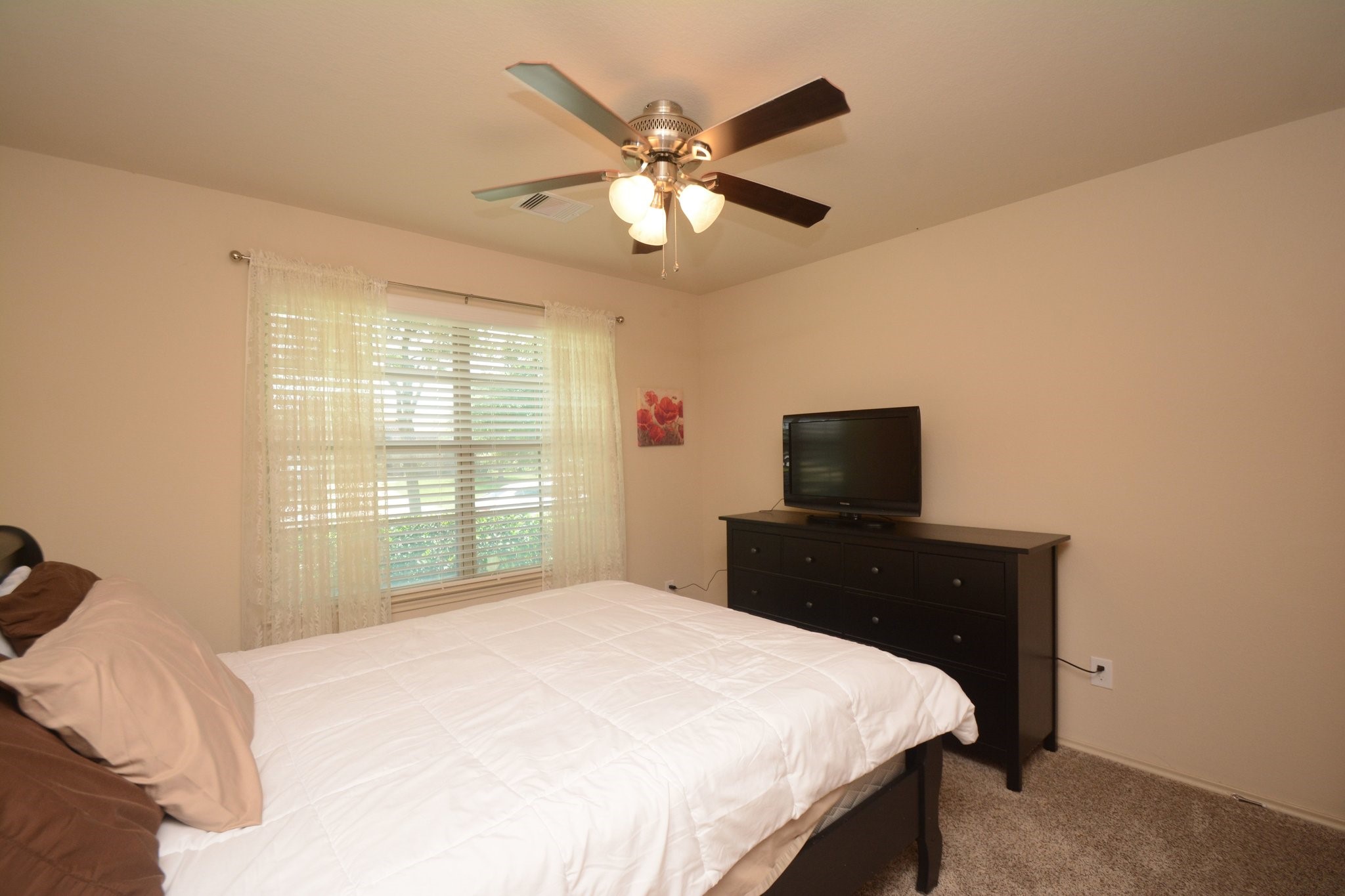 23318 Dukes Run Drive Spring, TX 77373 - Photo 20 of 41 Cozy bedroom with neutral walls and carpet, featuring a ceiling fan and a large window for natural light. Includes space for a comfortable bed and a dresser with room to spare.