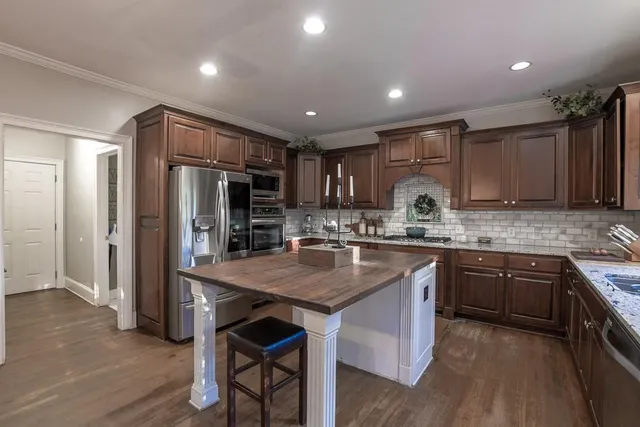 a kitchen with stainless steel appliances granite countertop wooden cabinets a sink a stove a dining table and chairs