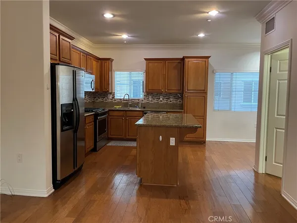 a kitchen with stainless steel appliances granite countertop a refrigerator a sink dishwasher a stove with wooden cabinets and wooden floor