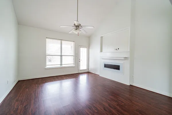an empty room with wooden floor ceiling fan and windows
