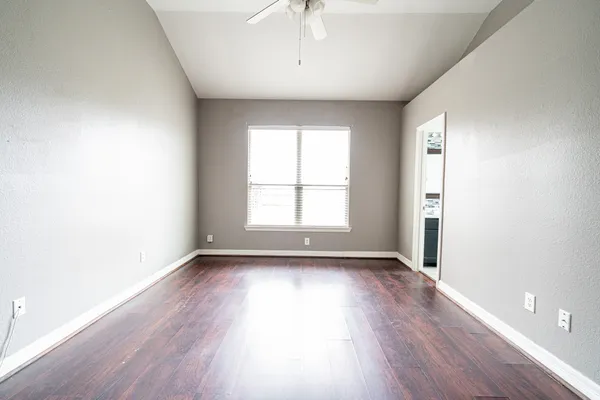 an empty room with wooden floor chandelier fan and windows