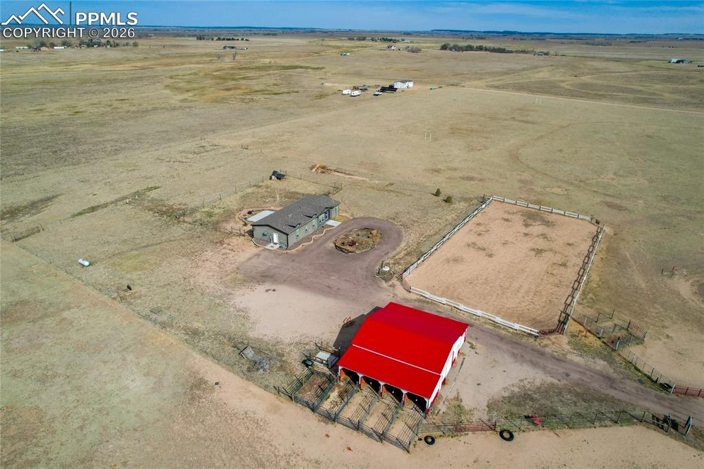 7880 J D Johnson Road Peyton, CO 80831 - Photo 38 of 50 Expansive property featuring a red-roofed barn with stalls, a fenced riding arena, a single-story residence, and a circular driveway