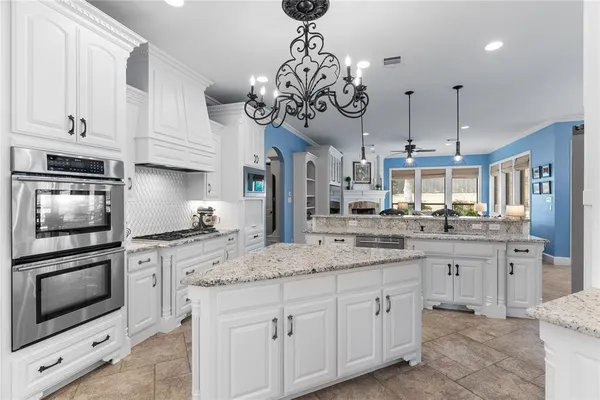 a large kitchen with stainless steel appliances kitchen island granite countertop a refrigerator a sink dishwasher a stove and white cabinets with wooden floor