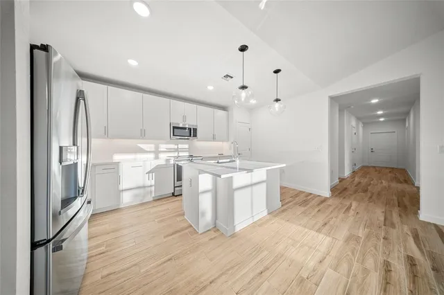 a kitchen with stainless steel appliances granite countertop a refrigerator a sink dishwasher a stove and white countertops with wooden floor