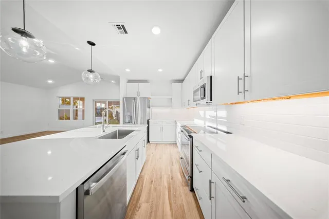 a large kitchen with stainless steel appliances kitchen island a large counter top and a chandelier