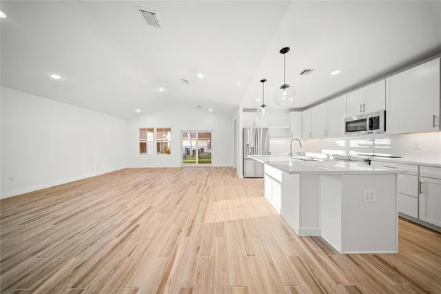 a large white kitchen with kitchen island a sink dishwasher a stove a refrigerator and white cabinets with wooden floor