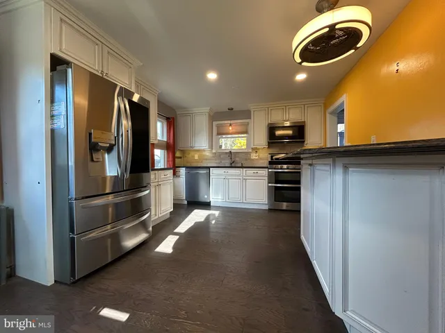 a kitchen with stainless steel appliances granite countertop a refrigerator a stove and a sink with wooden floor