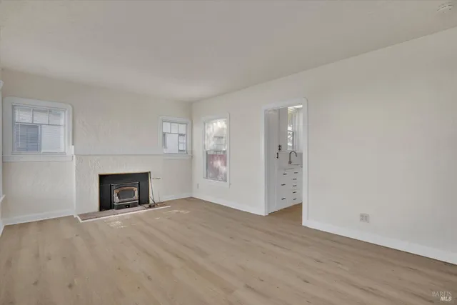 an empty room with wooden floor fireplace and windows