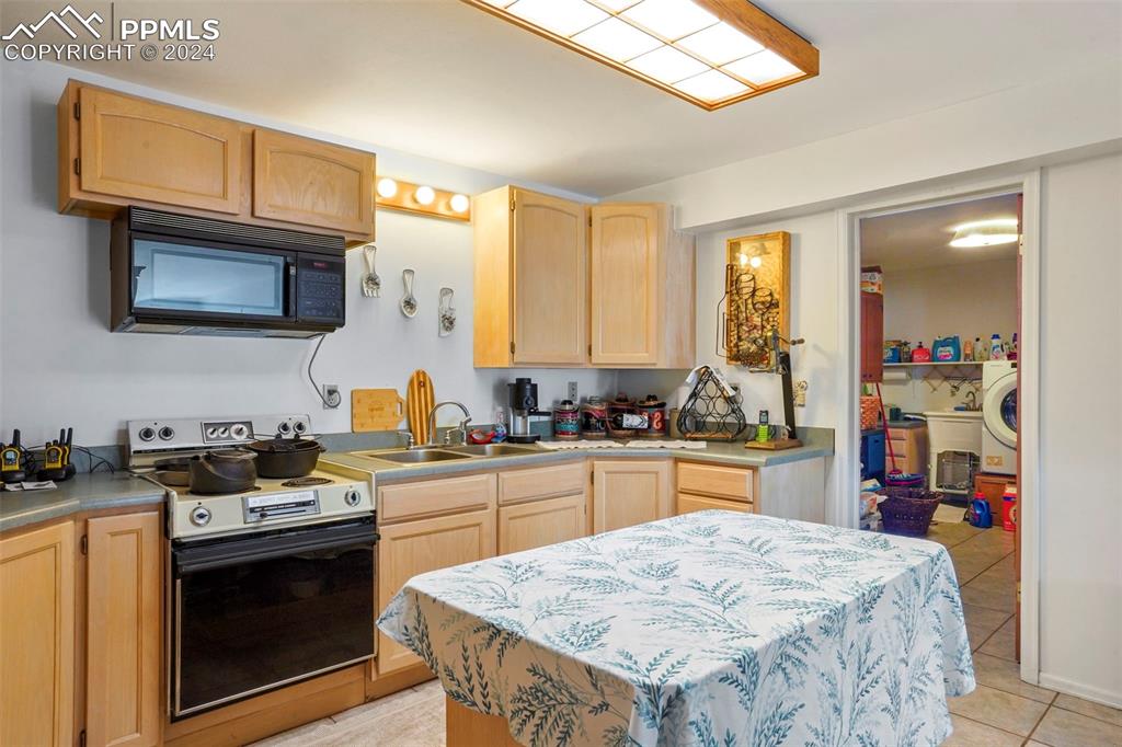 8155 Soap Weed Road Calhan, CO 80808 - Photo 27 of 39 Kitchen featuring sink, white electric range oven, light tile patterned floors, washer / clothes dryer, and light brown cabinetry