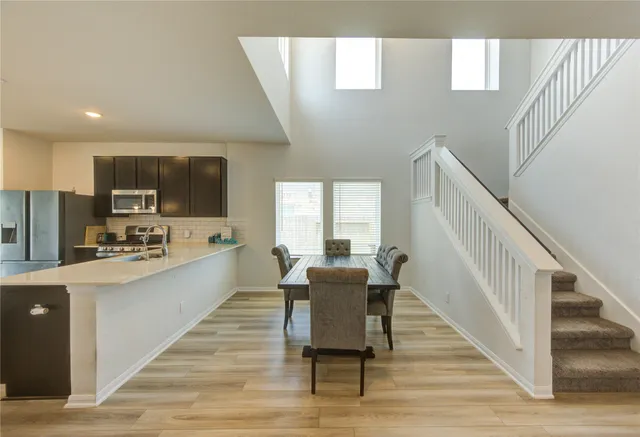 a living room with stainless steel appliances furniture a dining table wooden floor and a kitchen view