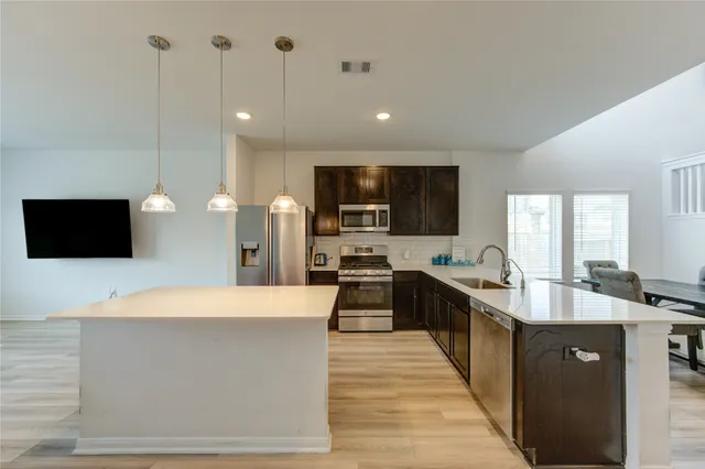 a large kitchen with kitchen island a stove a sink dishwasher and a refrigerator with wooden floor