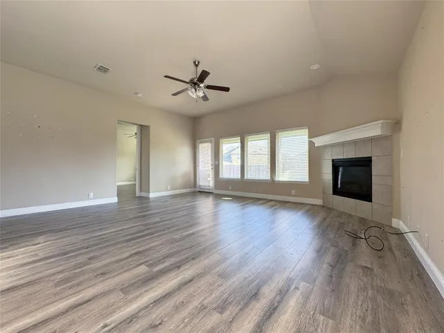 an empty room with wooden floor a ceiling fan and windows