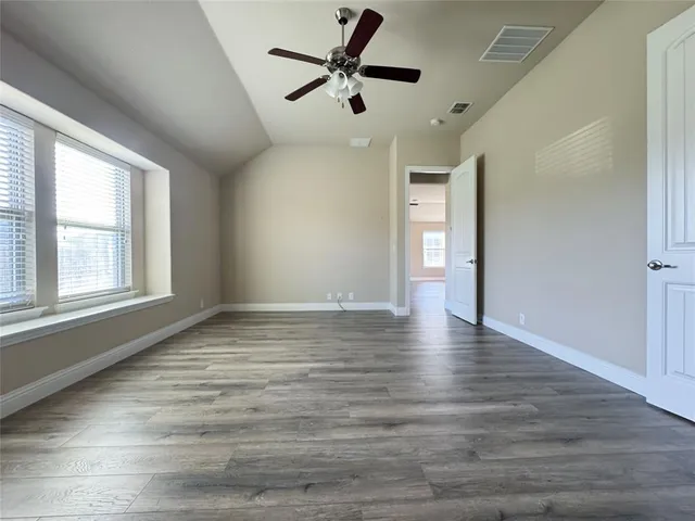 an empty room with wooden floor a kitchen view and a window