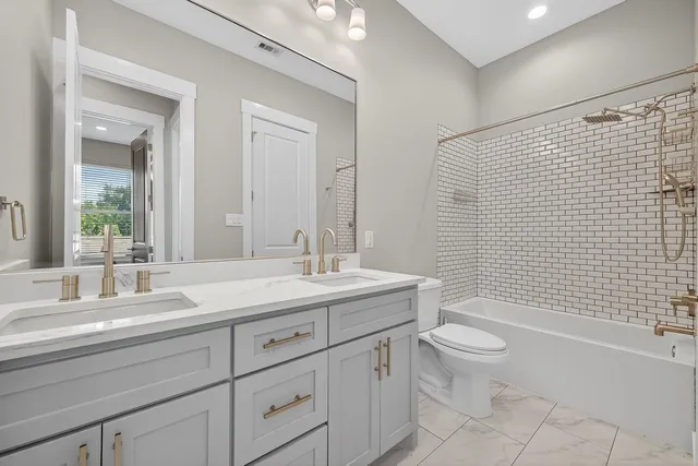 a bathroom with a granite countertop toilet a sink a mirror a bathtub and shower