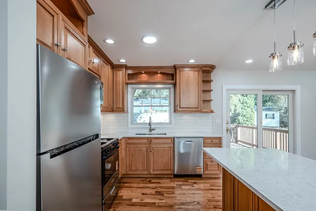 a kitchen with stainless steel appliances granite countertop a refrigerator a sink dishwasher a stove and white countertops with wooden floor