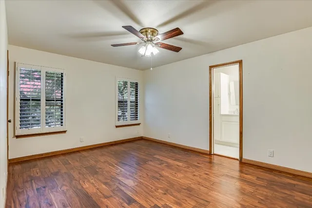 an empty room with wooden floor chandelier fan and windows