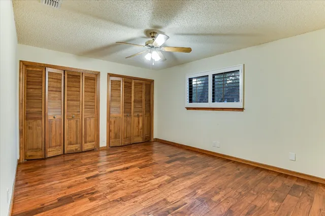 a view of an empty room with wooden floor and a ceiling fan