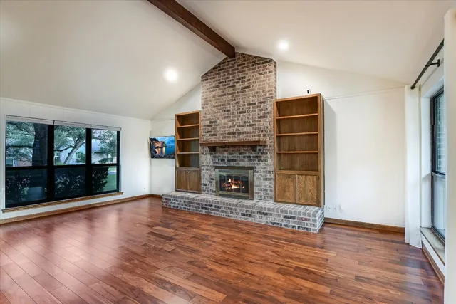 a view of an empty room with wooden floor fireplace and a window