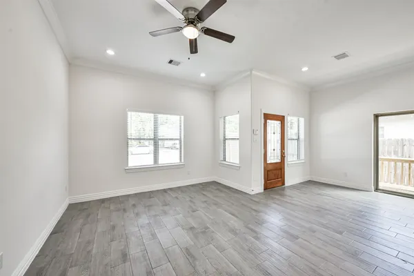 an empty room with wooden floor a ceiling fan and windows