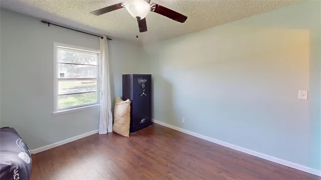an empty room with wooden floor chandelier fan and windows