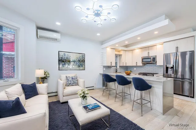 a living room with stainless steel appliances furniture a rug and a kitchen view