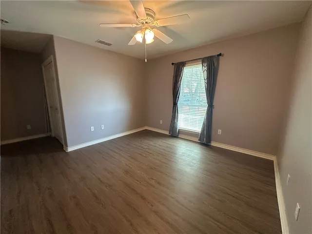 an empty room with wooden floor chandelier fan and windows