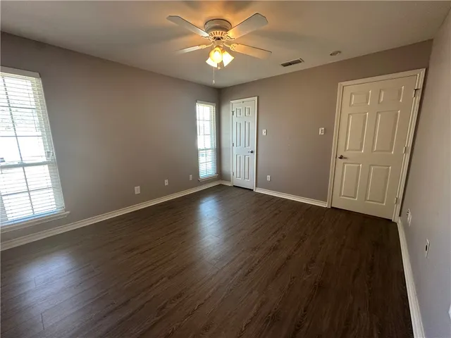 an empty room with wooden floor and windows with curtains