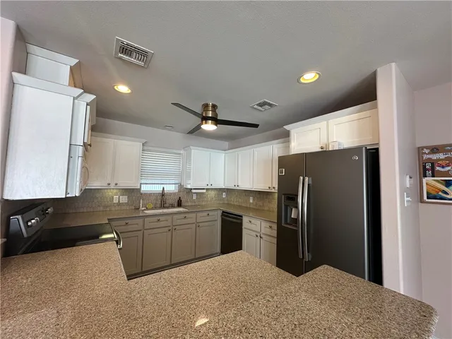 a kitchen with stainless steel appliances granite countertop a refrigerator a sink a stove a oven with white cabinets and wooden floor