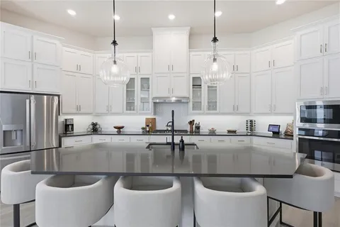 a kitchen with stainless steel appliances granite countertop a sink a stove a refrigerator and white cabinets with wooden floor