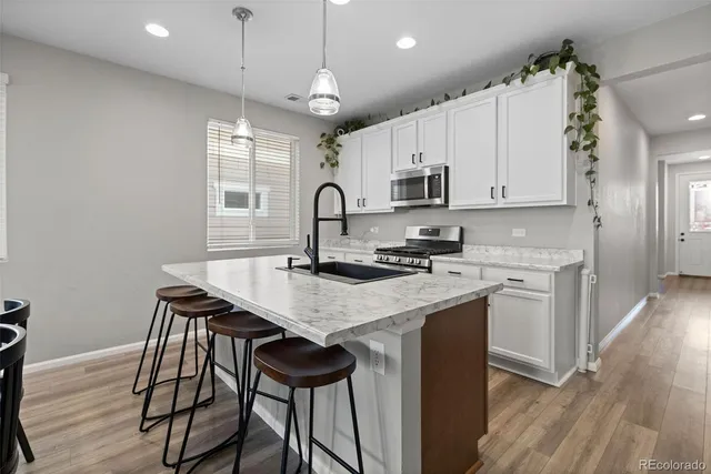 a kitchen with kitchen island a stove a sink a refrigerator and white cabinets with wooden floor