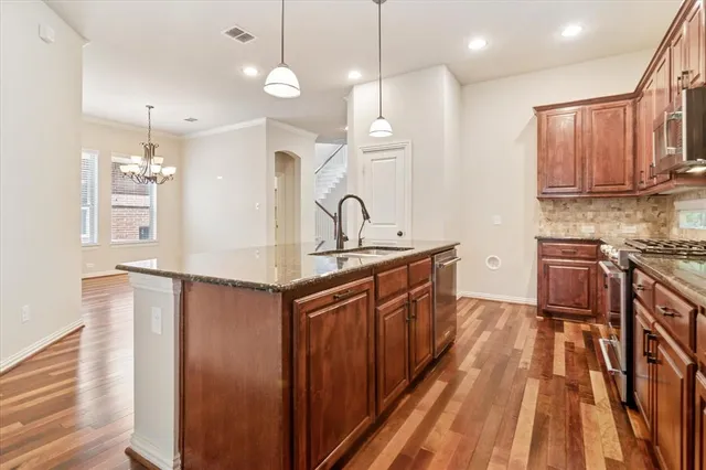 a kitchen with stainless steel appliances granite countertop a refrigerator a sink dishwasher a stove and white countertops with wooden floor