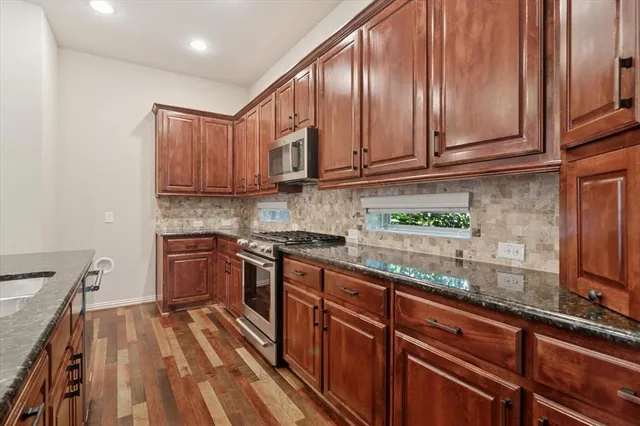 a kitchen with stainless steel appliances granite countertop a sink a stove and a wooden floors
