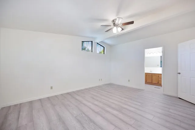 a view of an empty room with wooden floor and a ceiling fan