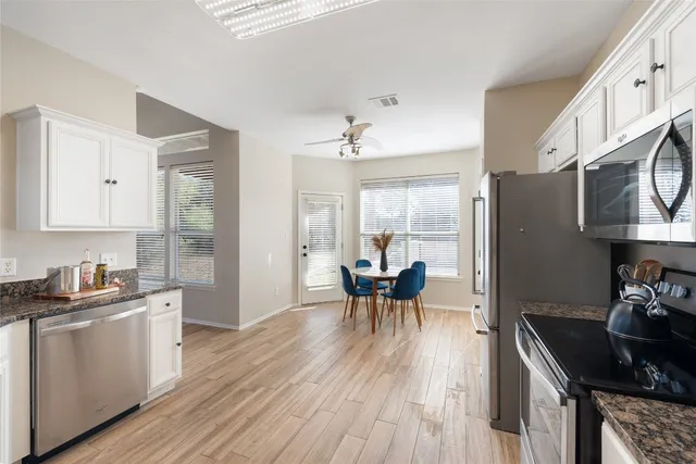 a kitchen with stainless steel appliances granite countertop a stove top oven a sink a dining table and chairs with wooden floor