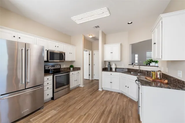 a large kitchen with stainless steel appliances a refrigerator a stove top oven a sink dishwasher and wooden floor